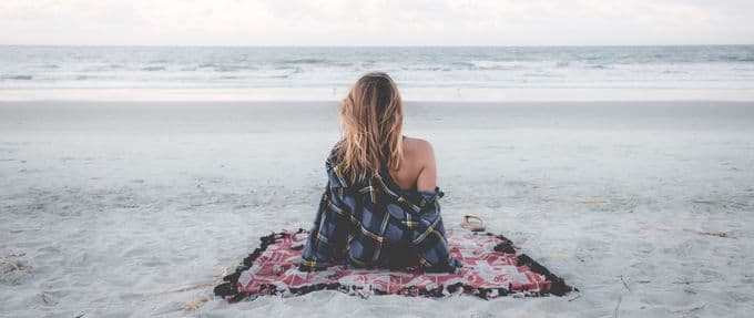 Woman sits on a blanket at a beach.