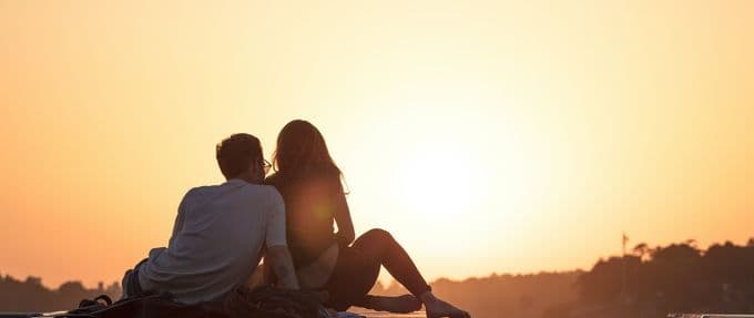 A man and a woman sit under a sunset embracing.